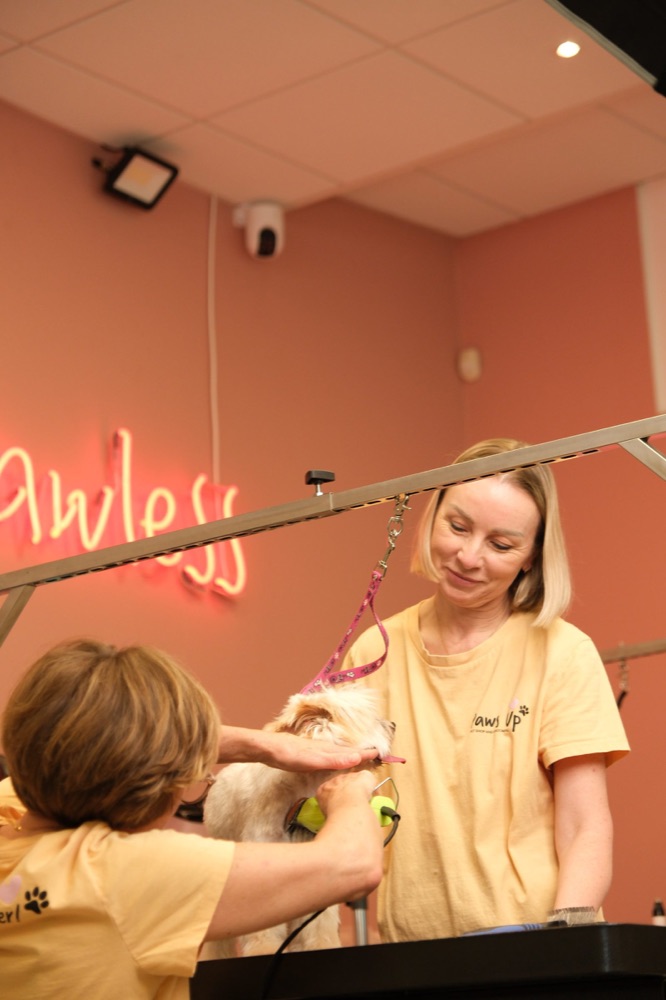 Team member in the PawsUp salon under a neon sign